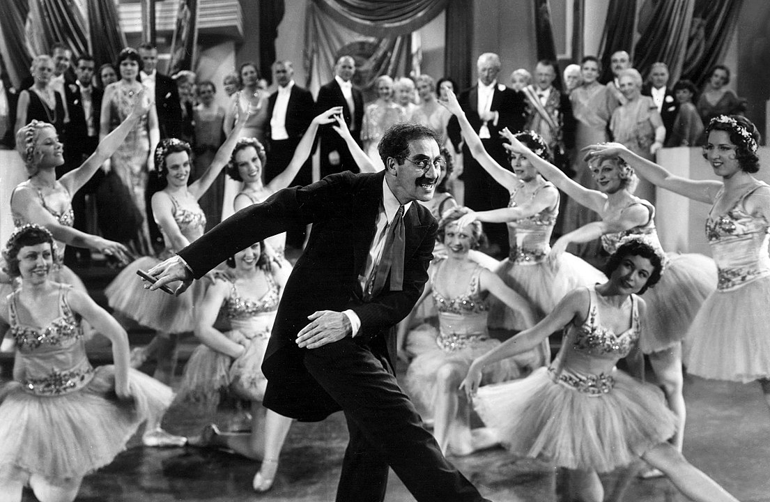Groucho Marx, cigar in hand, dances with a number of ladies.